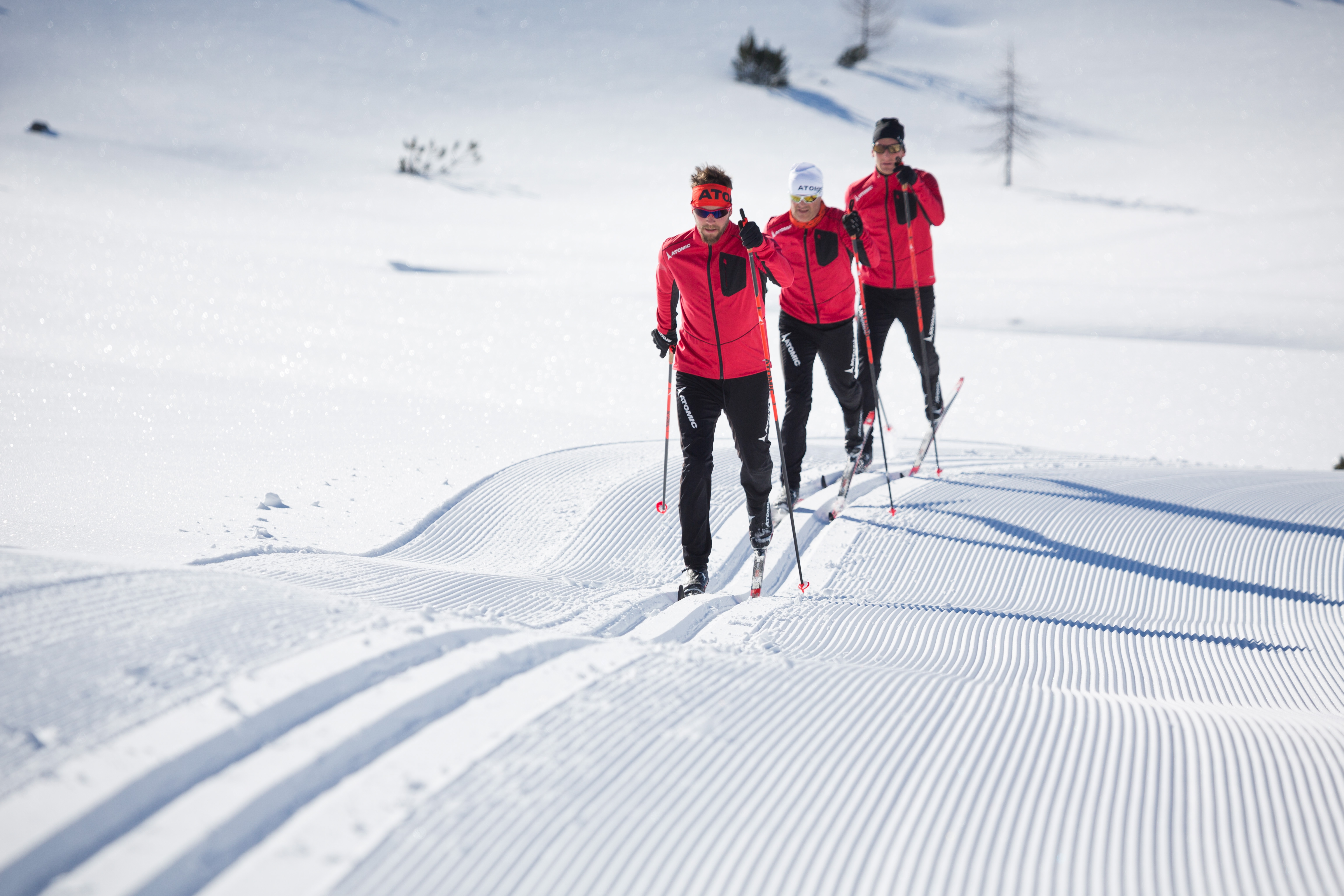 Un groupe de skieur de fond se suivent un à un sur une piste de ski de fond. Il y a beaucoup de rythme dans leur mouvement