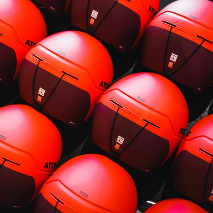 Une multitude de casques de ski Atomic orange vif et marron foncé, alignés en rangées.
